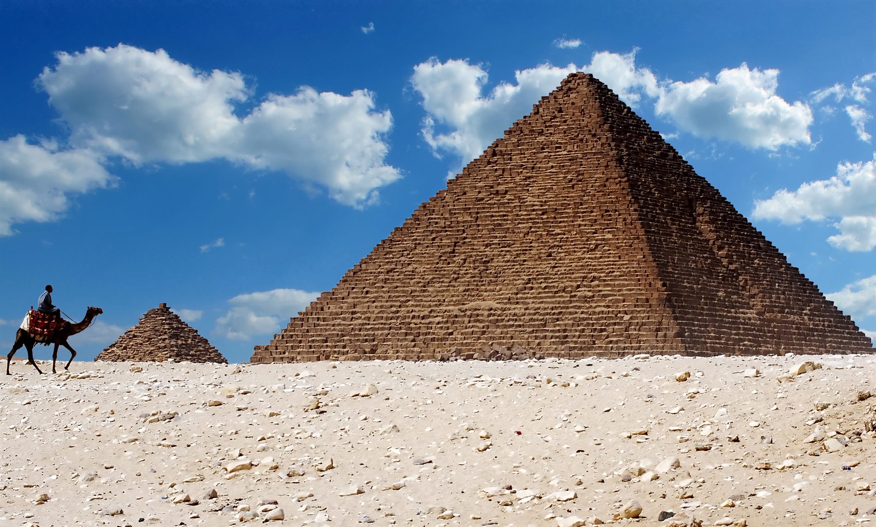 Pyramid in the desert with a camel rider passing